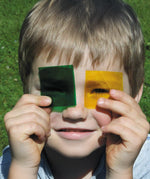 Child holding a green and yellow Kraul colour slide near the eyes showing their transparency.