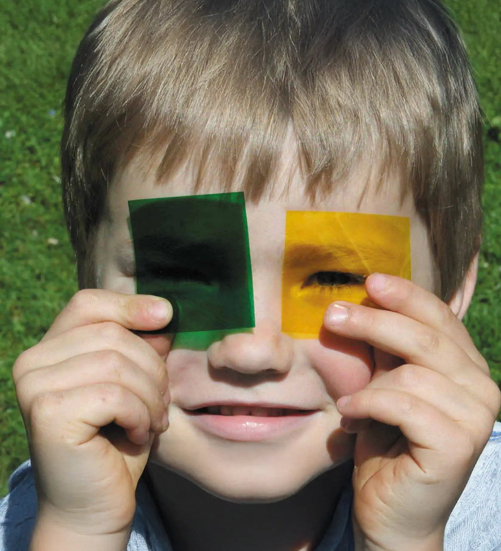 Child holding a green and yellow Kraul colour slide near the eyes showing their transparency.