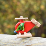 A green felt Kraul Little Passenger Doll placed on a red Bajo fire engine helicopter. These pose-able dolls are perfect to fit inside smaller toy vehicles and for use with the Kraul cable cars.
