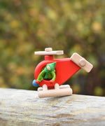 A green felt Kraul Little Passenger Doll placed on a red Bajo fire engine helicopter. These pose-able dolls are perfect to fit inside smaller toy vehicles and for use with the Kraul cable cars.