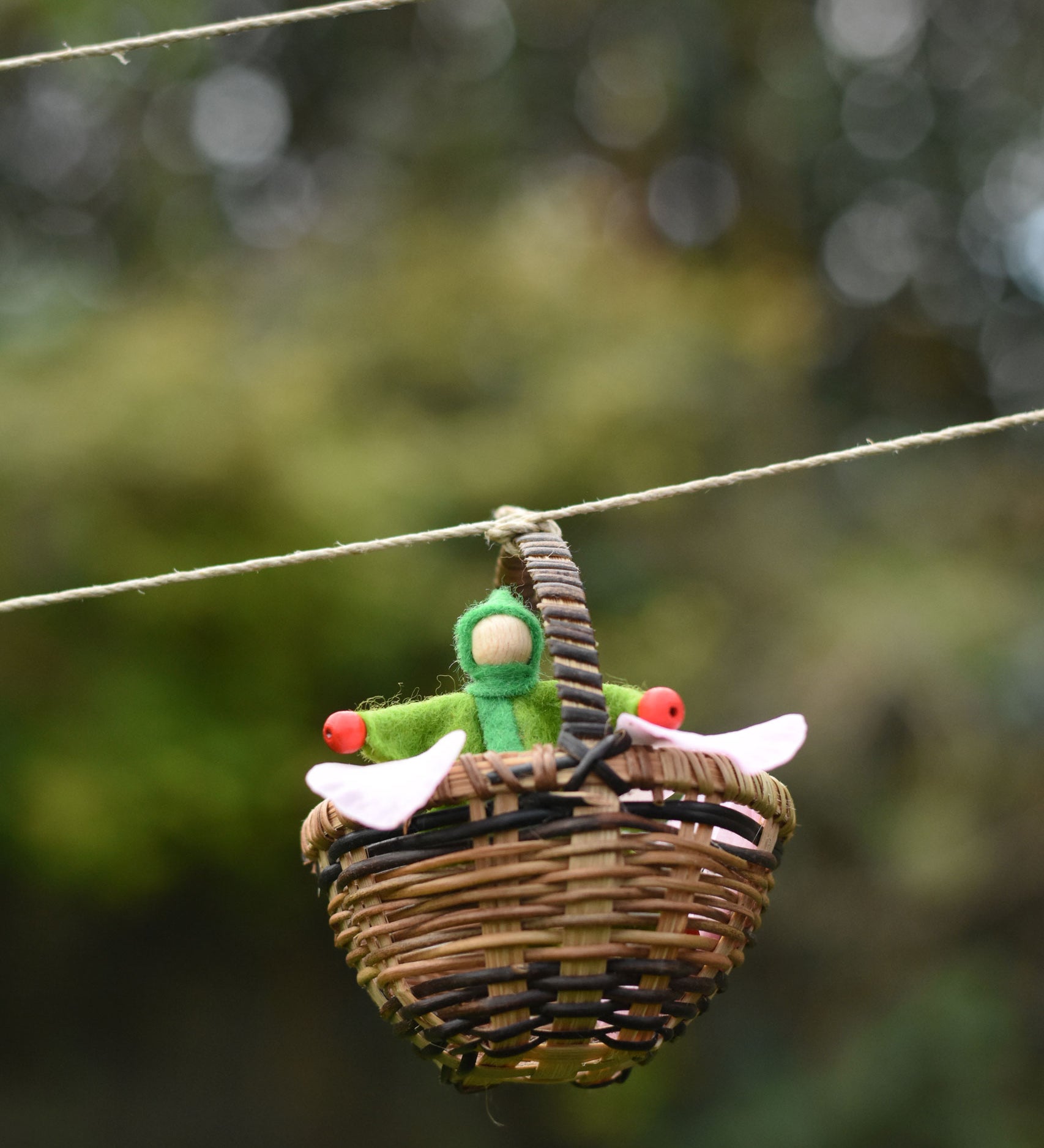 A green felt Kraul Little Passenger Doll in a Kraul basket. These pose-able dolls are perfect to fit inside smaller toy vehicles and for use with the Kraul cable cars.