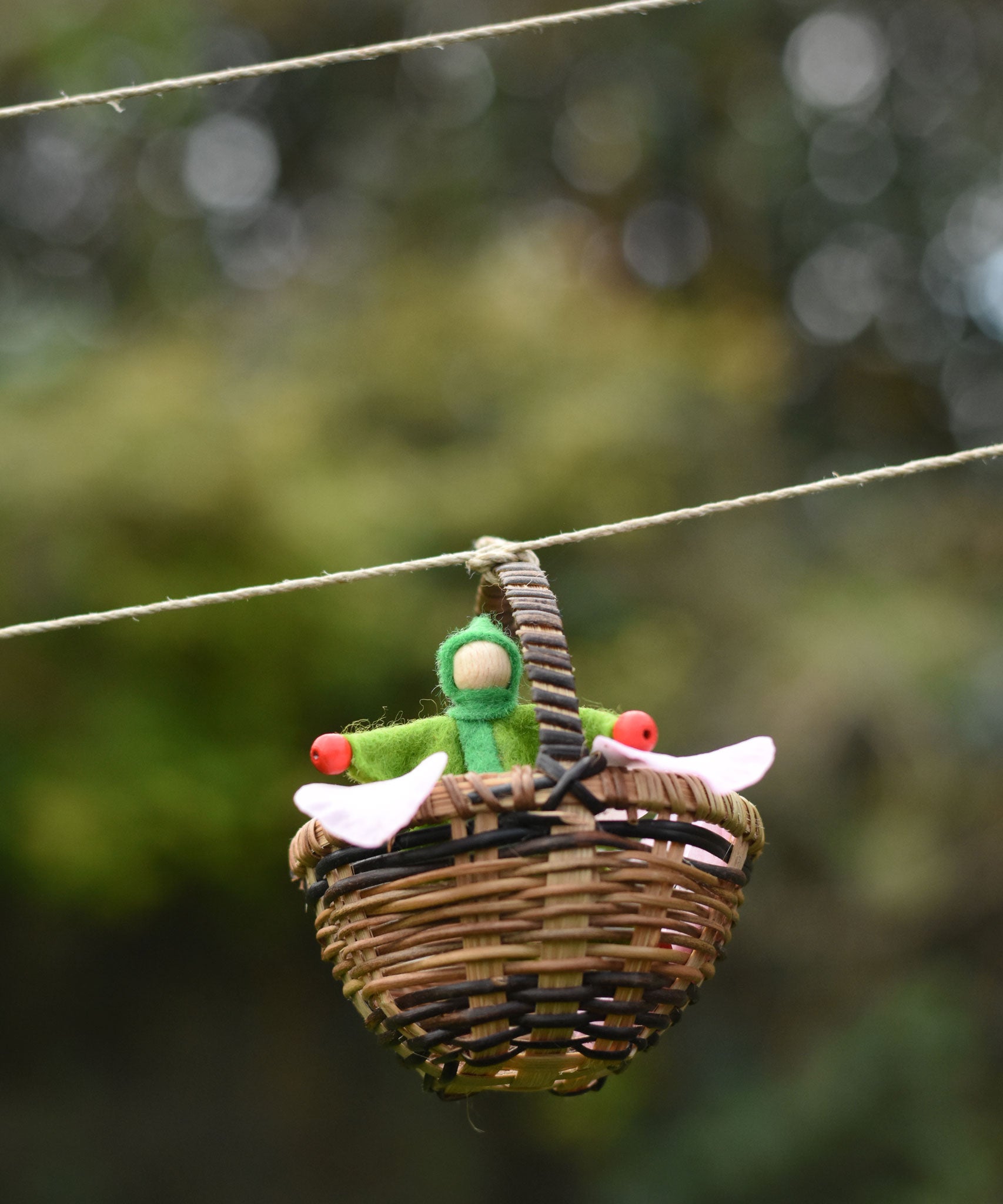 A green felt Kraul Little Passenger Doll in a Kraul basket. These pose-able dolls are perfect to fit inside smaller toy vehicles and for use with the Kraul cable cars.