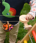 A close up of a child's hand turning the wheel on the Kraul DIY Basket Cable Car STEM Kit.  An adult's hand can be seen turning the wheel control in the background. 