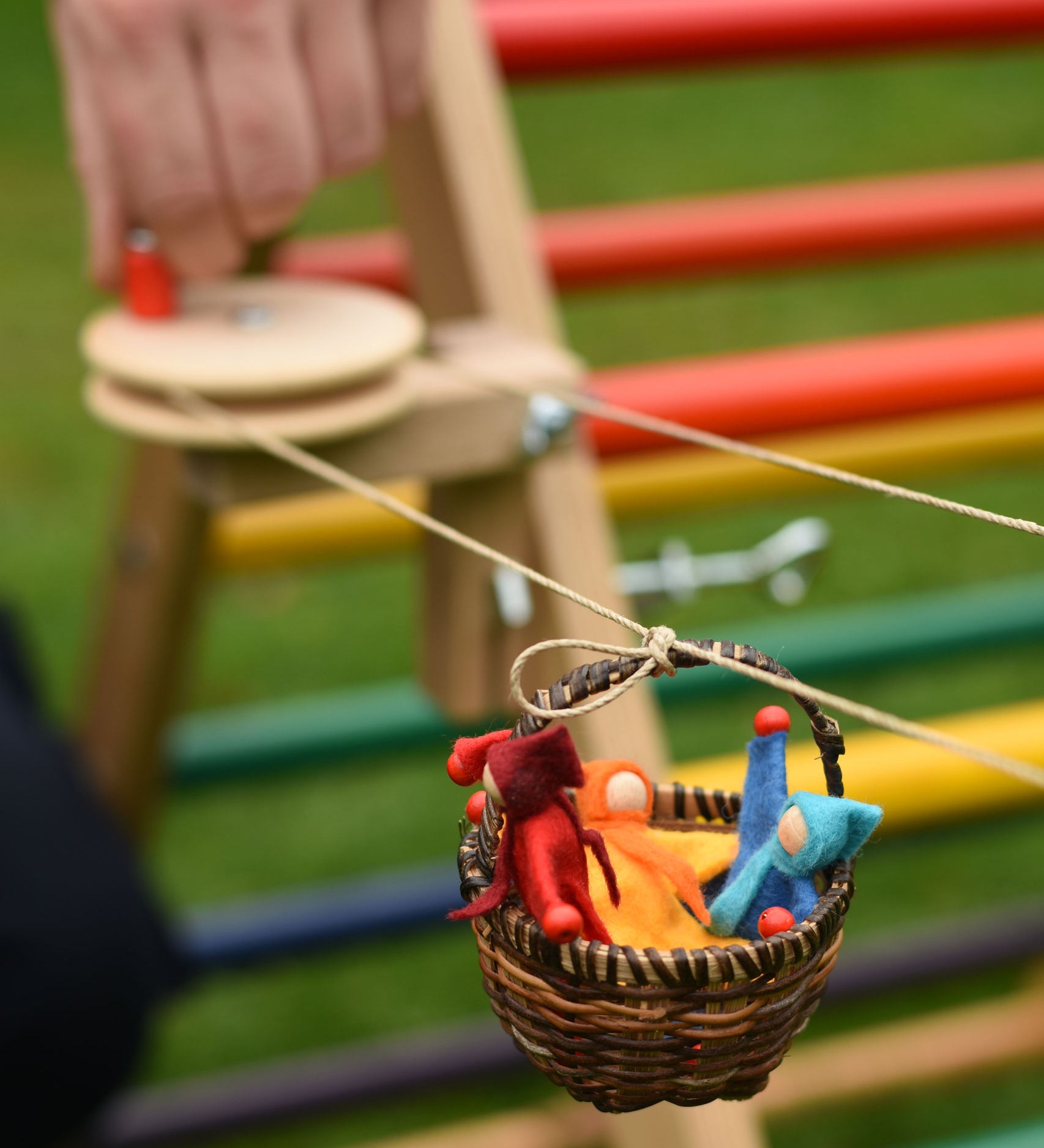 A close up of one of the wicker baskets on the rope of the Kraul DIY Basket Cable Car STEM Kit.  An adult's hand can be seen turning the wheel control in the background. 