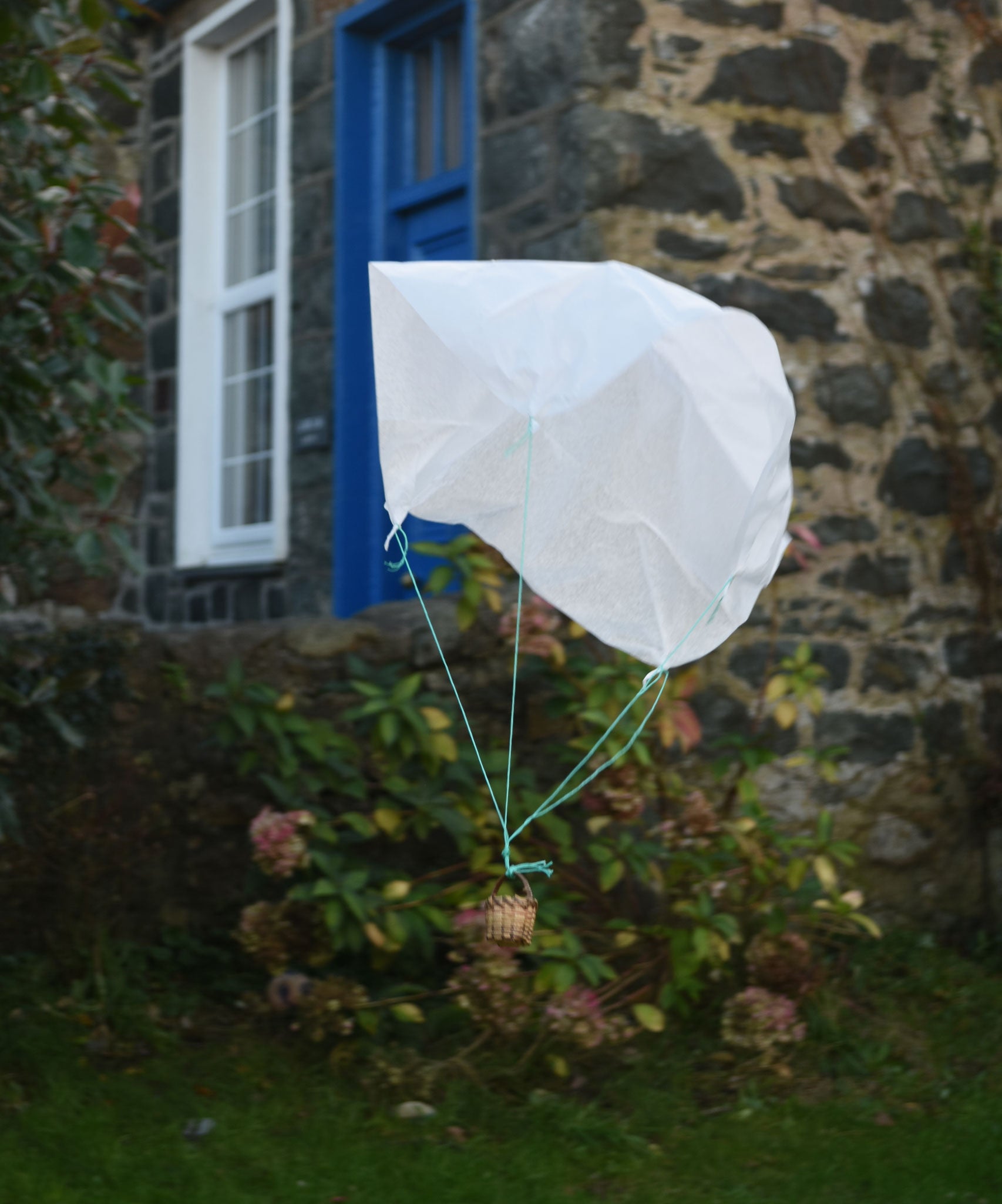 A DIY paper parachute made using the Kraul parachute kit floating down in mid air.  Kraul offers a range of thoughtful science toys that bring natural forces to life through real-world exploration and play.