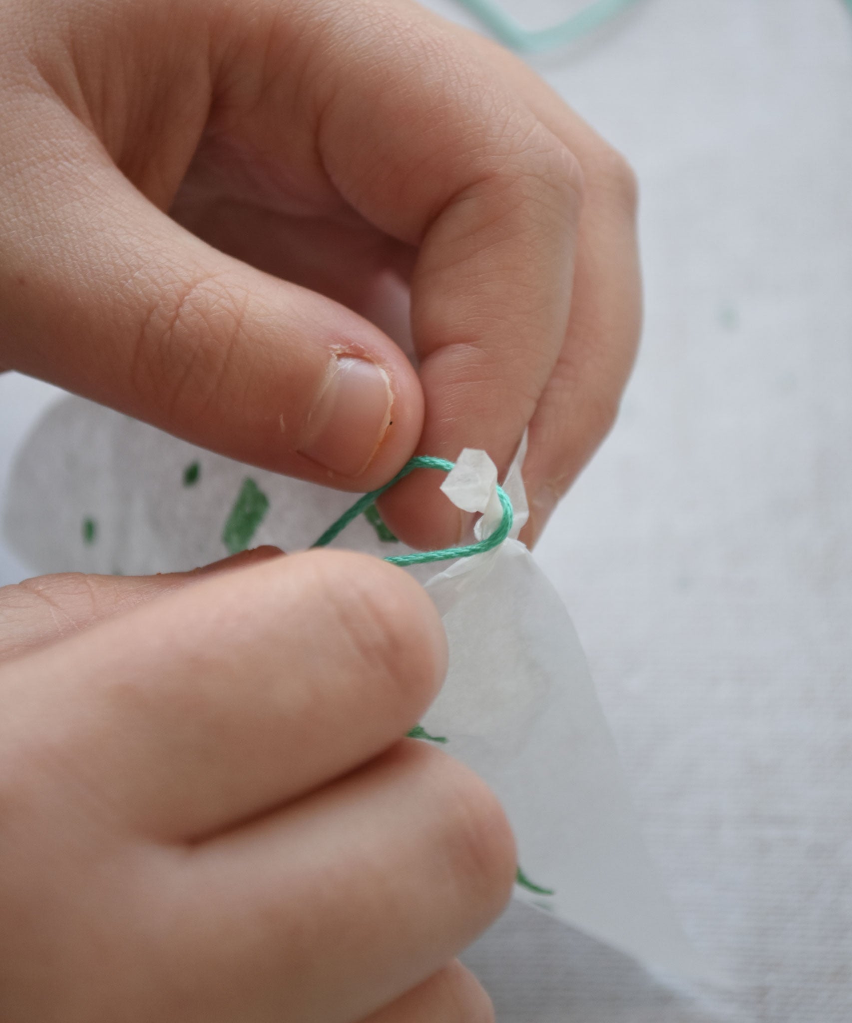 A close up of a child's hand tying the thread onto a corner of the silk paper ready to make a parachute with the kit. The kit contains papers, thread and a mini basket. Kraul offers a range of thoughtful science toys that bring natural forces to life through real-world exploration and play.