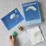 The contents of the Kraul parachute kit laid out. The kit contains papers, thread and a mini basket. Kraul offers a range of thoughtful science toys that bring natural forces to life through real-world exploration and play.