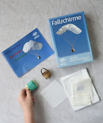 The contents of the Kraul parachute kit laid out. The kit contains papers, thread and a mini basket. Kraul offers a range of thoughtful science toys that bring natural forces to life through real-world exploration and play.