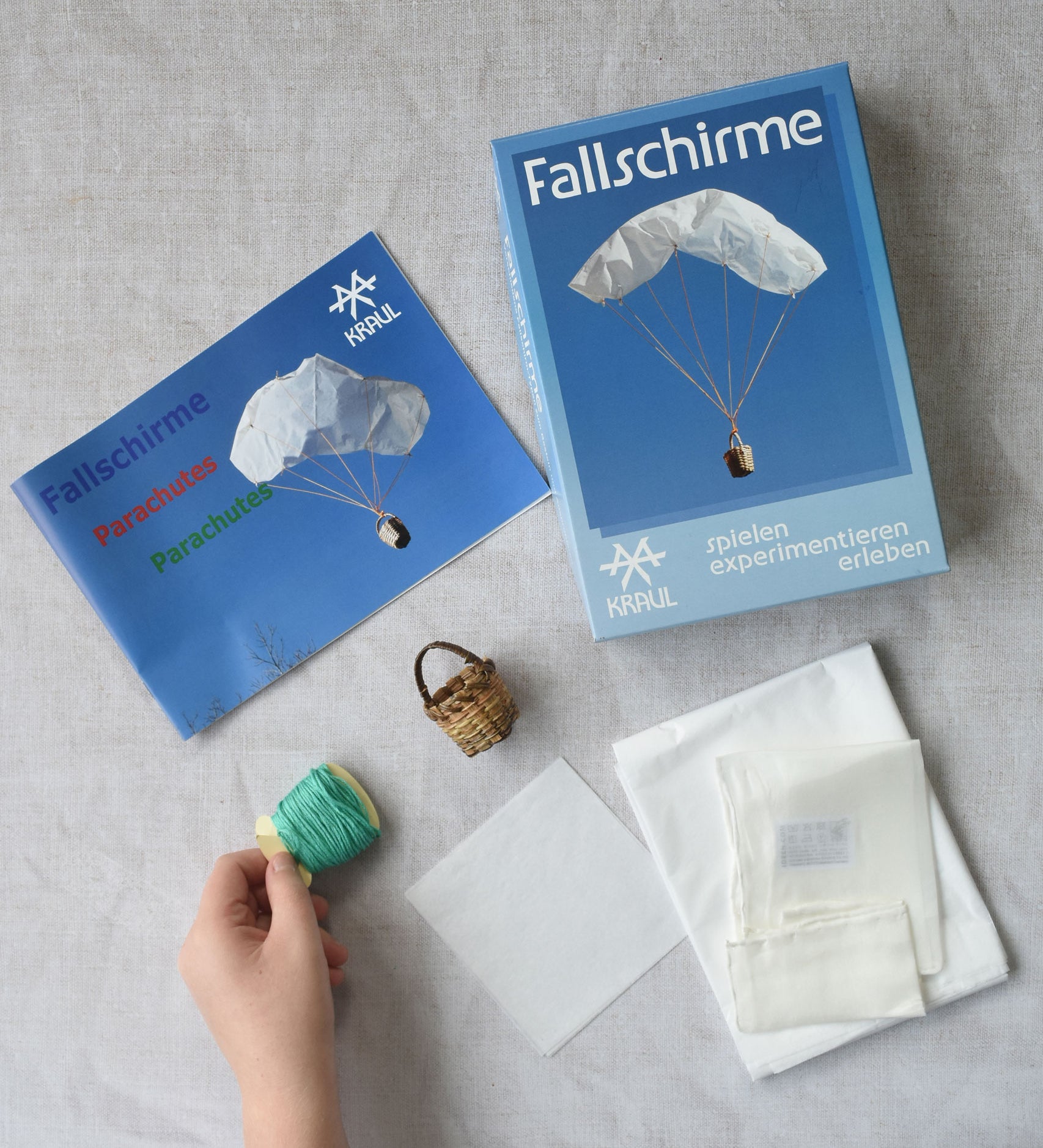 The contents of the Kraul parachute kit laid out. The kit contains papers, thread and a mini basket. Kraul offers a range of thoughtful science toys that bring natural forces to life through real-world exploration and play.