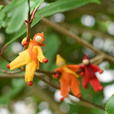 A yellow felt Kraul Little Passenger Doll handing on a little branch on a tree. Other dolls can be seen in the background. These pose-able dolls are perfect to fit inside smaller toy vehicles and for use with the Kraul cable cars.