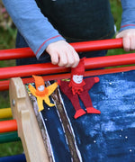 A small and large Kraul tumbling gnome placed on a Triclimb Miri slide covered by a Wonderie play cloth. A child's hand can be seen starting to push the large gnome. 