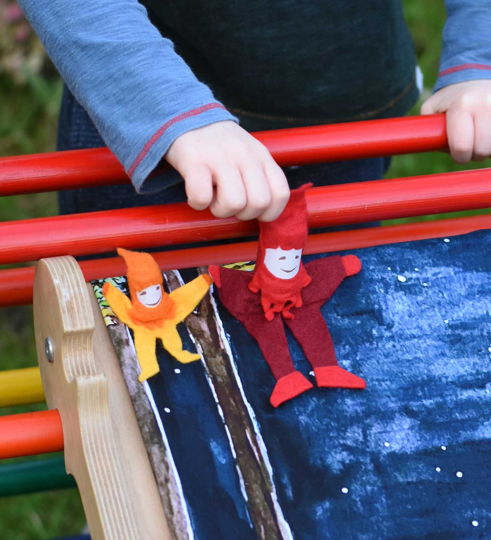 A small and large Kraul tumbling gnome placed on a Triclimb Miri slide covered by a Wonderie play cloth. A child's hand can be seen starting to push the large gnome. 