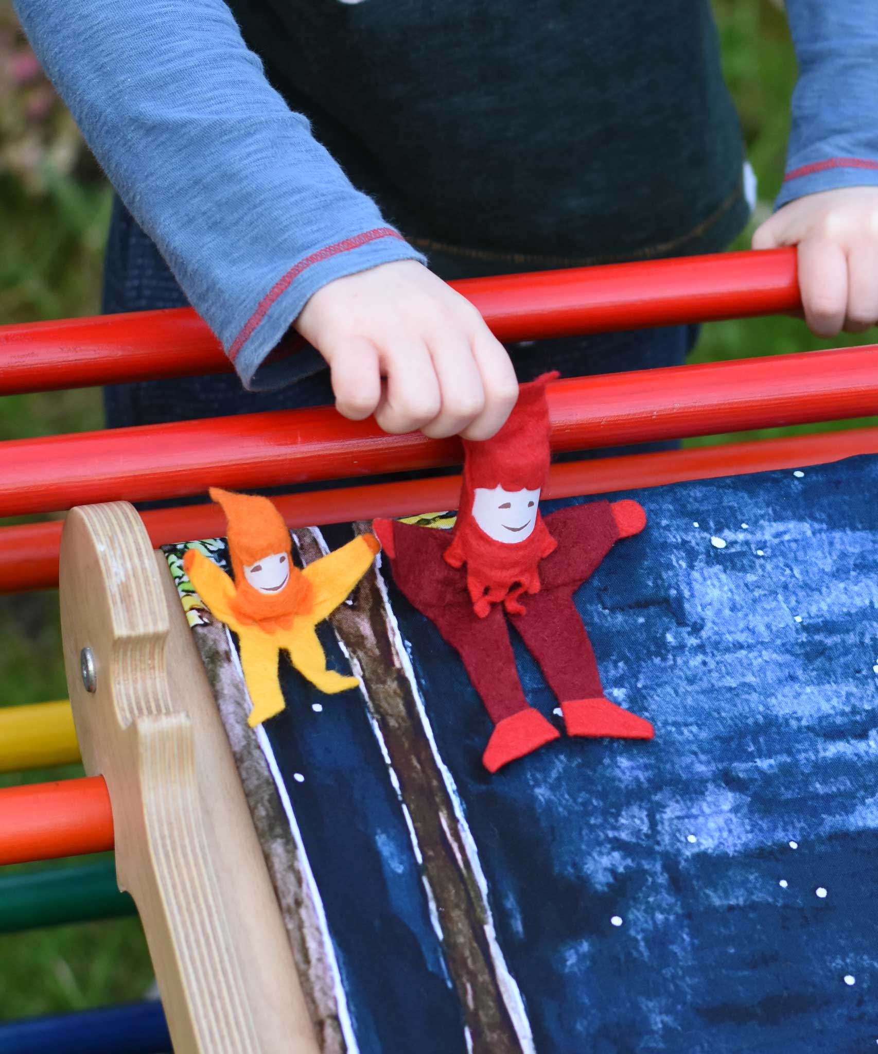 A small and large Kraul tumbling gnome placed on a Triclimb Miri slide covered by a Wonderie play cloth. A child's hand can be seen starting to push the large gnome. 