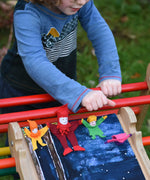 4 Kraul tumbling gnomes placed on a TriClimb Miri slide ready to be tumbled down. A child has pushed a pink coloured gome and it can be seen tumbling down in motion. These felt gnome dolls come in various colours and sizes.