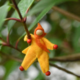 A yellow felt Kraul Little Passenger Doll placed on a branch of a tree. These pose-able dolls are perfect to fit inside smaller toy vehicles and for use with the Kraul cable cars.
