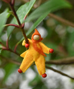 A yellow felt Kraul Little Passenger Doll placed on a branch of a tree. These pose-able dolls are perfect to fit inside smaller toy vehicles and for use with the Kraul cable cars.