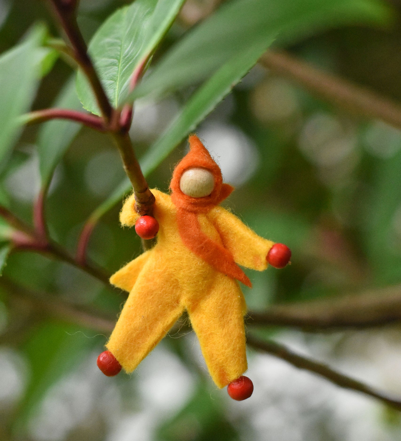 A yellow felt Kraul Little Passenger Doll placed on a branch of a tree. These pose-able dolls are perfect to fit inside smaller toy vehicles and for use with the Kraul cable cars.