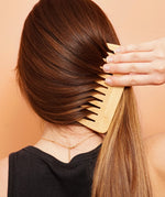 Woman combing long, shiny hair with a wooden comb after using Lamazuna keratin solid haircare for repair and strength.