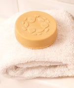 Lamazuna Keratin Repair Solid Shampoo Bar placed on a folded white towel, a round vegan shampoo bar for damaged or dull hair.
