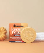 Lamazuna Keratin Repair Solid Shampoo Bar positioned in front of its box, a round 70g vegan shampoo bar for repairing and strengthening hair.