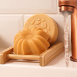 Lamazuna Keratin Shine solid conditioner bar resting in a wooden soap dish with the Keratin Repair shampoo bar behind it beside a running tap