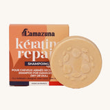 Lamazuna Keratin Repair Solid Shampoo Bar in front of its orange box, a round plant-based keratin shampoo for repairing dry or damaged hair.