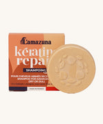 Lamazuna Keratin Repair Solid Shampoo Bar in front of its orange box, a round plant-based keratin shampoo for repairing dry or damaged hair.