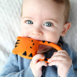 A baby holding and chewing on the Lanco Nalu the Tiger Teether