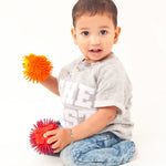 Child kneeling down on a white background holding 2 Lanco natural rubber toy hedgehogs