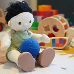 Close up of an Olli Ella Dinkum Doll toy sat on a white carpet with a Lanco natural rubber globe ball in its lap