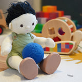 Close up of an Olli Ella Dinkum Doll toy sat on a white carpet with a Lanco natural rubber globe ball in its lap
