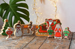 Lanka Kade wooden Christmas play set. 9 toy figures including Santa in his sleigh, Mrs Clause, Christmas Tree, Snowman, North Pole Sign, 2 Elves and 2 Reindeer placed on a wooden surface in the Babipur playroom. 