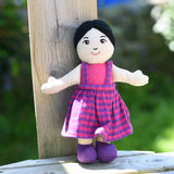 A close up of the face on the Lanka Kade Asian Girl Doll with White Skin and Black Hair leaning agaisnt a wooden post outdoors.