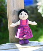 A close up of the face on the Lanka Kade Asian Girl Doll with White Skin and Black Hair leaning agaisnt a wooden post outdoors.