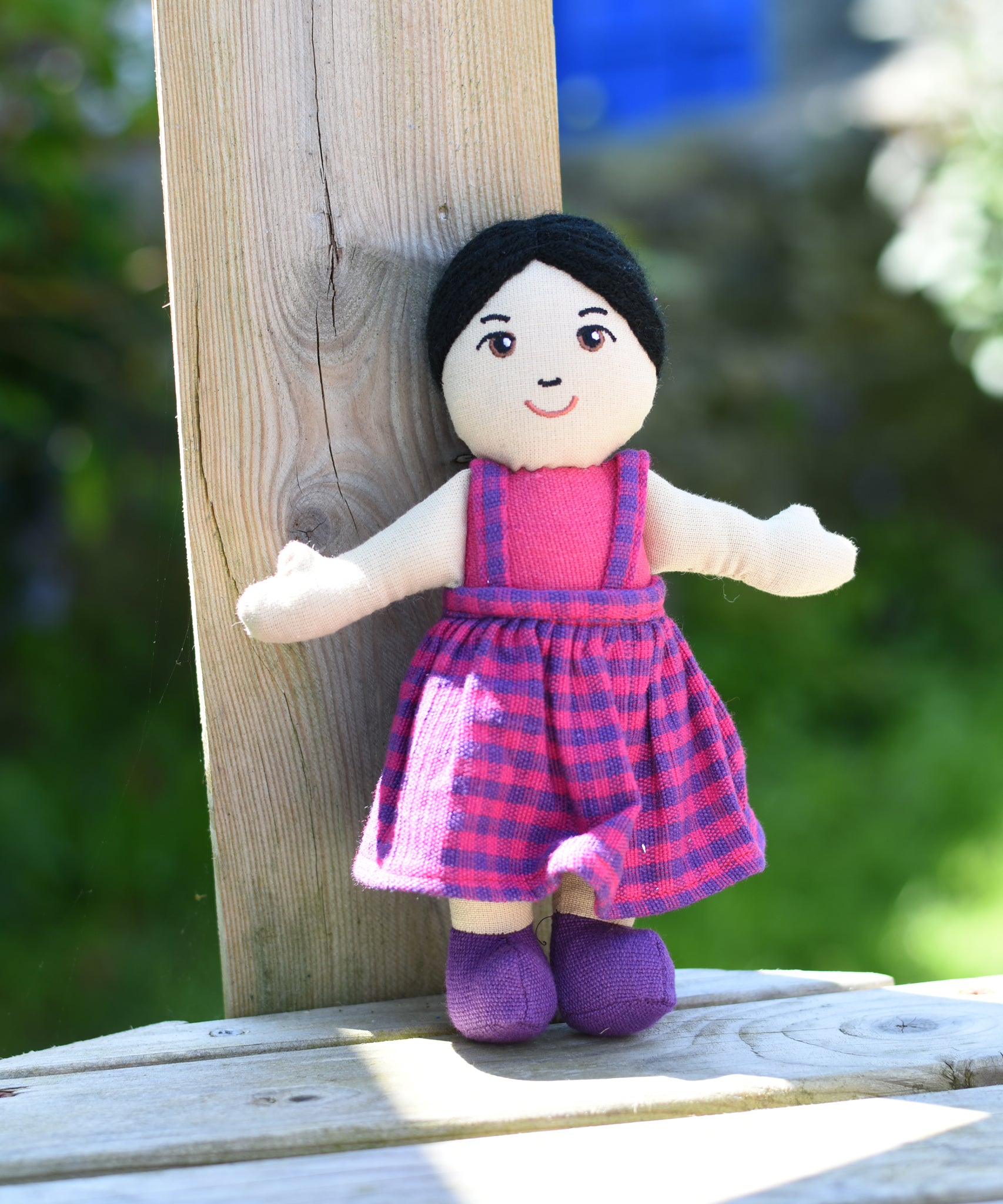 A close up of the face on the Lanka Kade Asian Girl Doll with White Skin and Black Hair leaning agaisnt a wooden post outdoors.