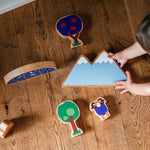 Looking down at a child playing with the Lanka Kade Babipur moel mountain toy and other dan y ser wooden toys on a wooden floor