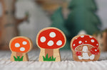 Lanka Kade and Babipur collaboration orange and red spotted toadstool and Lanka Kade Toadstool figures placed on a striped tablecloth. on 