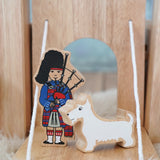 Lanka Kade wooden bagpiper standing next to a white scottie figure on a  castle  drawbridge