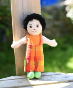A Lanka Kade Boy Doll with White Skin and Black Hair leaning against a wooden post outdoors.