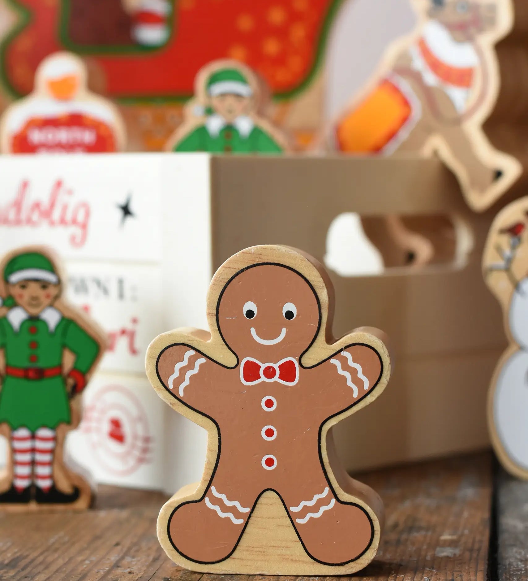 Lanka Kade gingerbread man wooden toy figure placed on a wooden surface in the Babipur playroom with a wooden crate filled with other Christmas figures in the background.