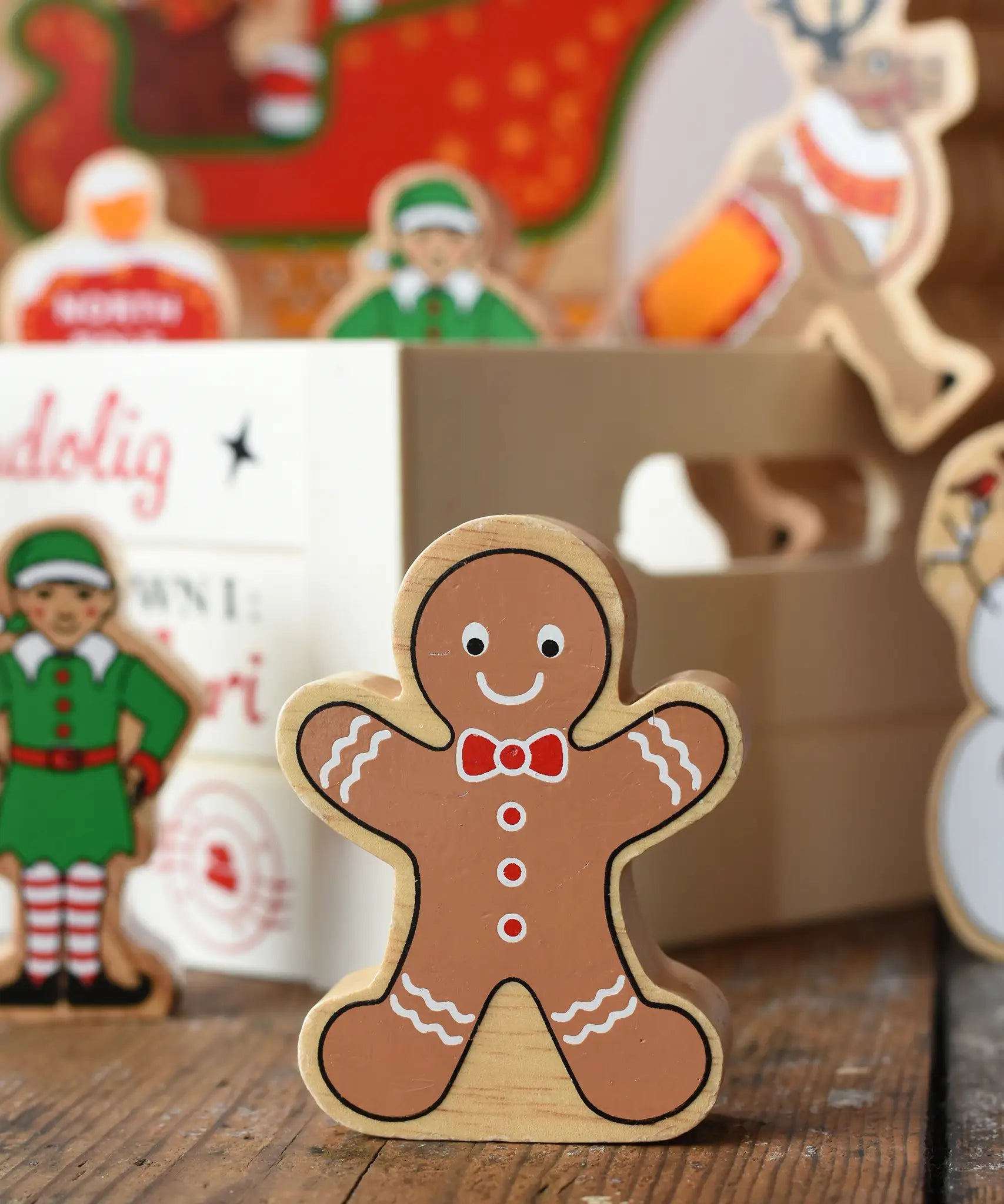 Lanka Kade gingerbread man wooden toy figure placed on a wooden surface in the Babipur playroom with a wooden crate filled with other Christmas figures in the background.