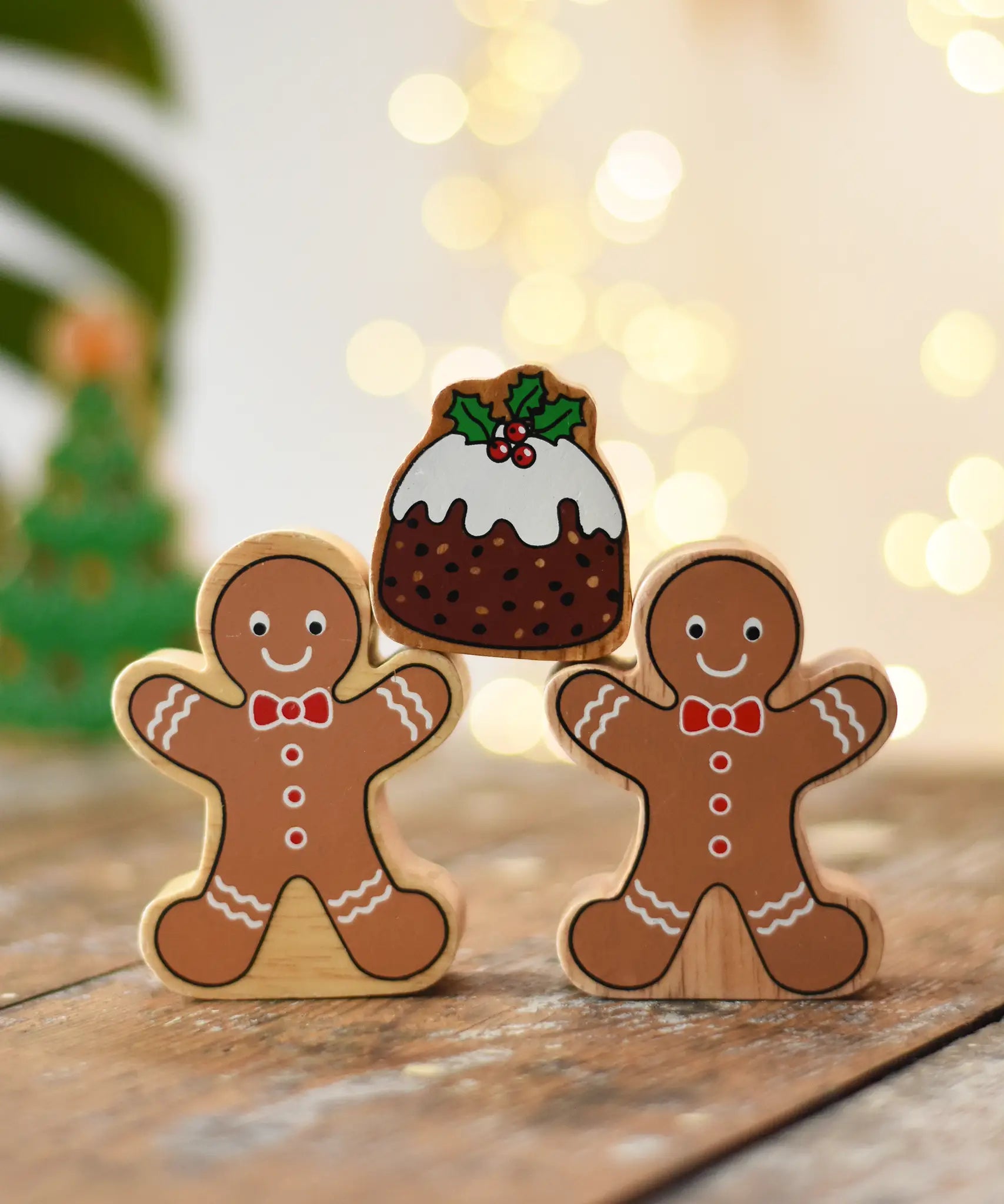 Two Lanka Kade gingerbread men wooden toy figure placed on a wooden surface in the Babipur playroom balancing a Christmas pudding on their arms.
