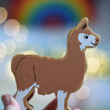 A Lanka Kade brown and white Llama wooden toy figure in an adult's hand. These wooden toy figures are part of a huge range of Lanka Kade fair trade, wooden toys available here at Babipur.