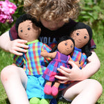 A child cuddling a Lanka Kade doll family, dad, mum and girl. The family all have brown skin and black hair. 
