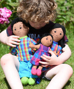 A child cuddling a Lanka Kade doll family, dad, mum and girl. The family all have brown skin and black hair. 