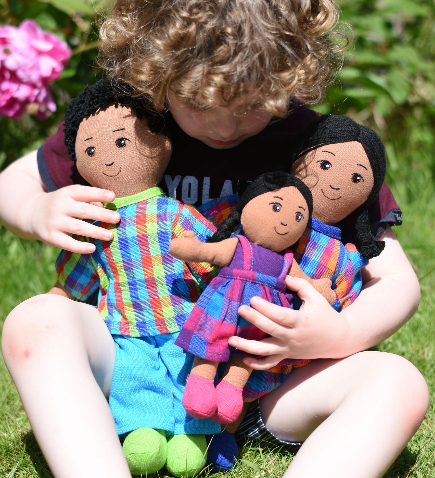 A child cuddling a Lanka Kade doll family, dad, mum and girl. The family all have brown skin and black hair. 