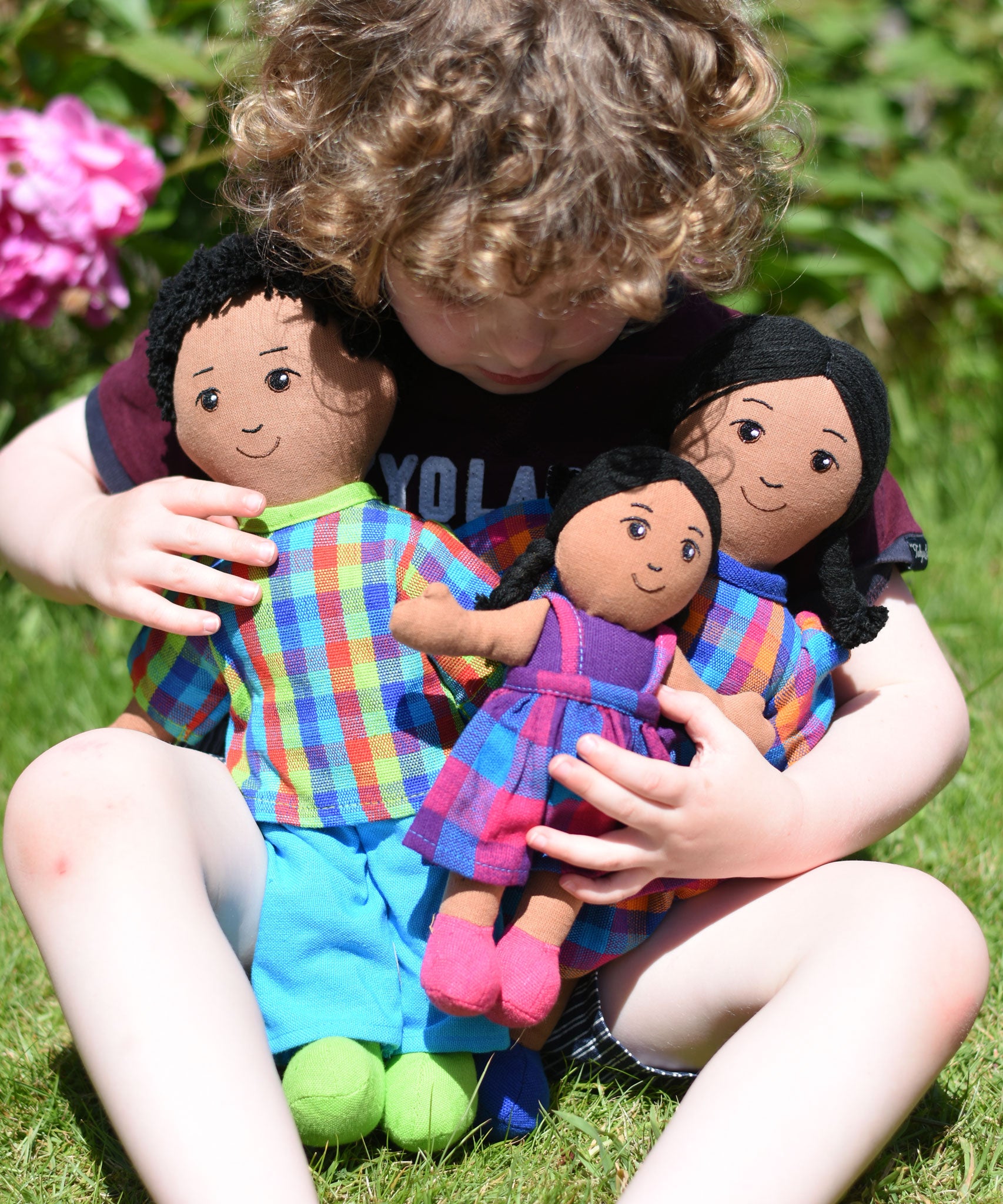 A child cuddling a Lanka Kade doll family, dad, mum and girl. The family all have brown skin and black hair. 