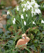 Lanka Kade brown bunny rabbit wooden toy figure placed on grass in front of a bunch of snowdrops. 