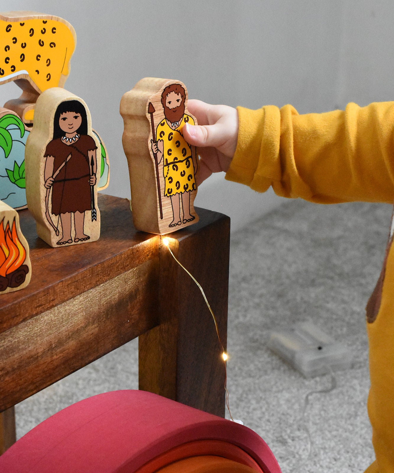 A child holding the cave fan figure from the Lanka Kade Prehistoric Playset. A play set that contains 8 wooden figure and scenery pieces. These wooden toy figures are part of a huge range of Lanka Kade fair trade, wooden toys available here at Babipur.