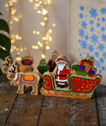 Lanka Kade wooden Christmas toy figures including Father Christmas,  red sleigh, Mrs Clause, North Pole Sign, Elf and 2 Reindeer placed on a wooden surface in the Babipur playroom.